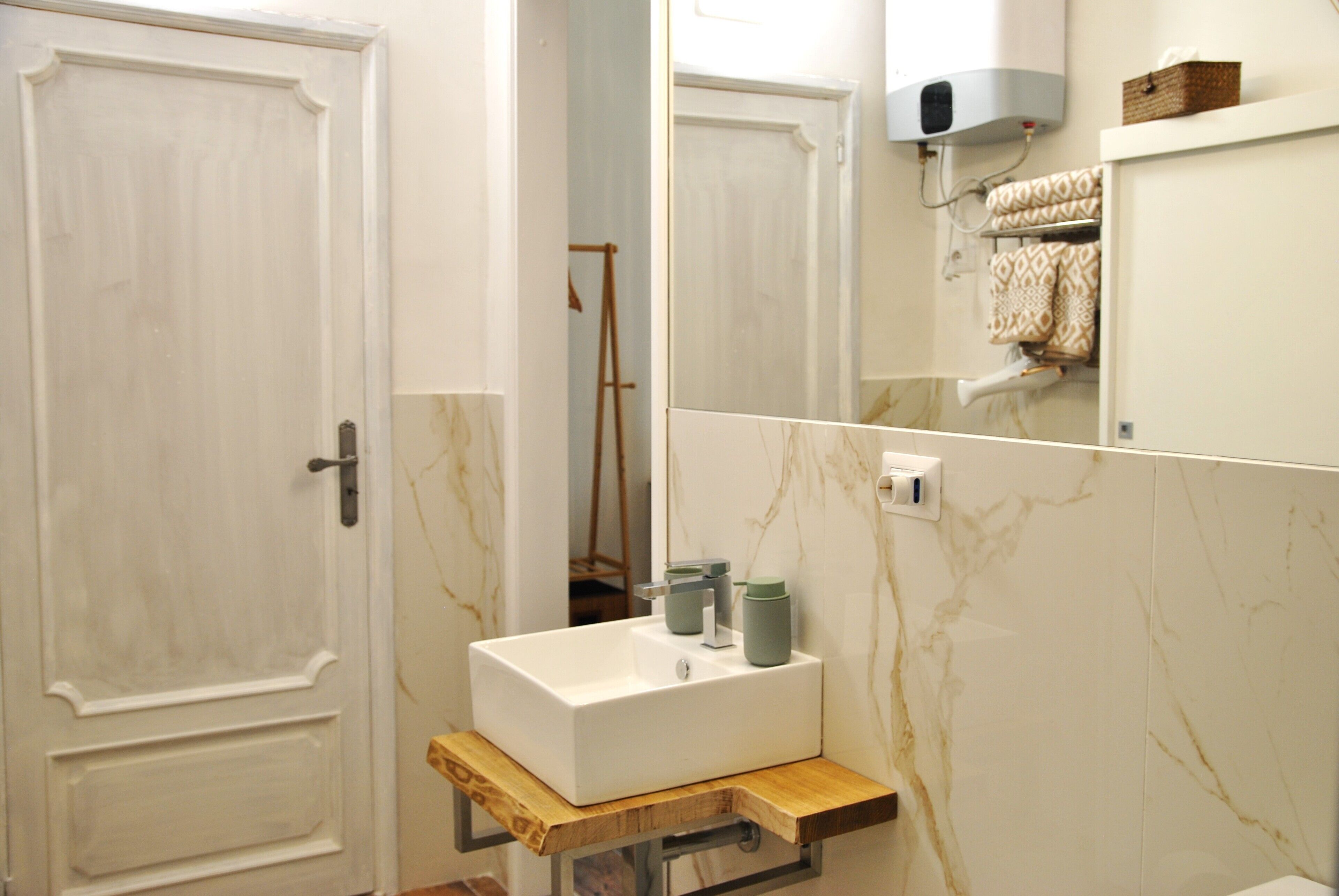 A bathroom with a white sink, a wooden shelf, a towel rack, and a mirror.