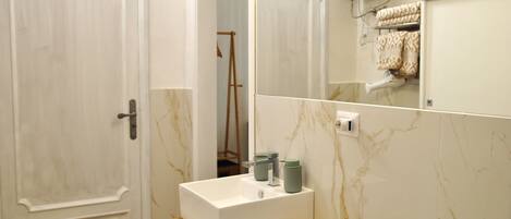 A bathroom with a white sink, a wooden shelf, a towel rack, and a mirror.