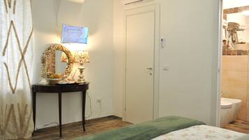 A bedroom with a bed, a bedside table with a lamp, a mirror, and a door to the bathroom.