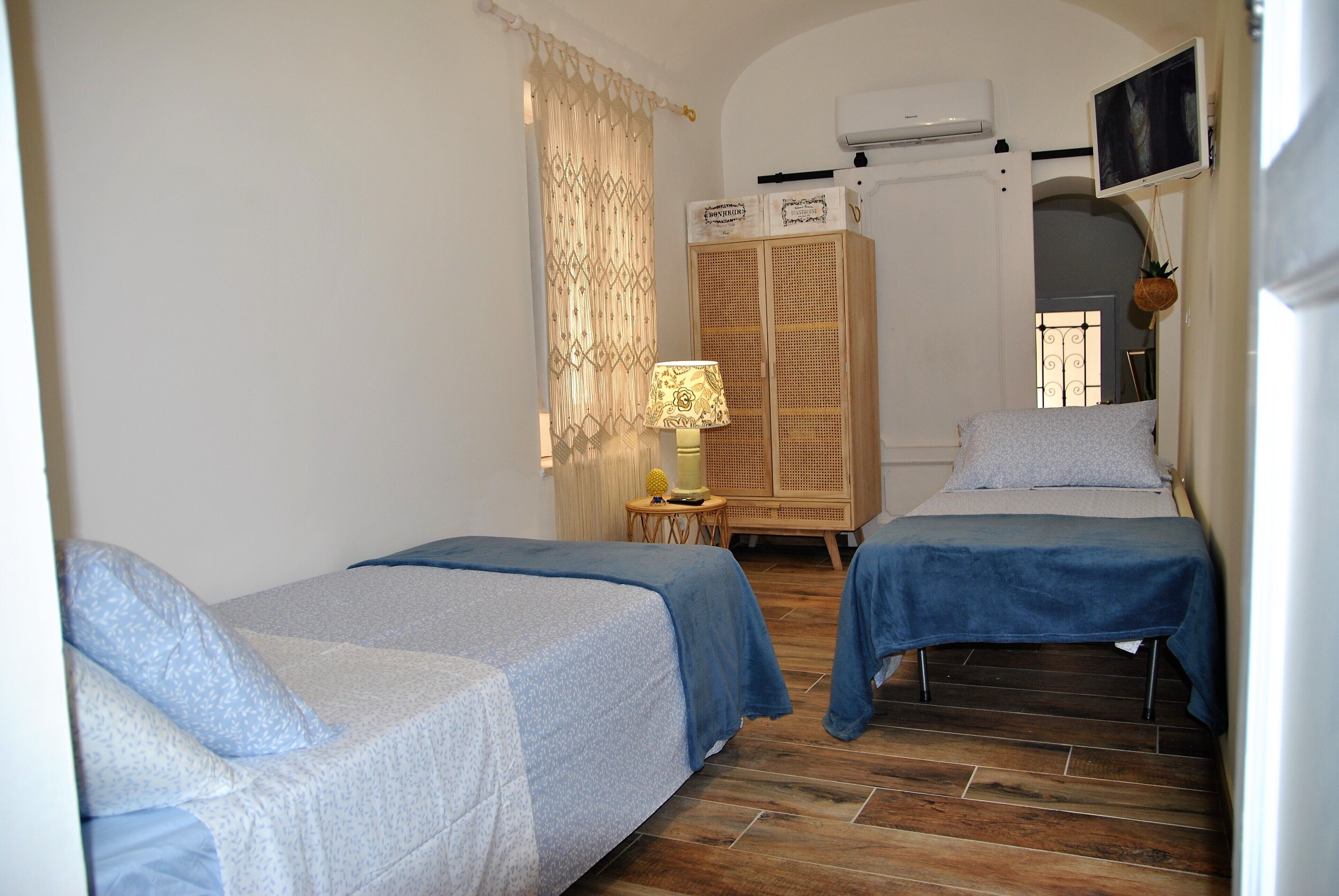 Una habitación con dos camas individuales, un armario de madera, una mesita con una lámpara y un televisor en la pared.