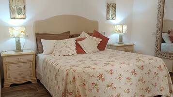 Un dormitorio con colcha estampada, dos lámparas de noche, suelo de madera y un espejo con marco decorativo.