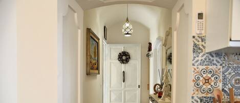 A hallway with a white door, a hanging light fixture, a fire extinguisher, and a tiled backsplash.