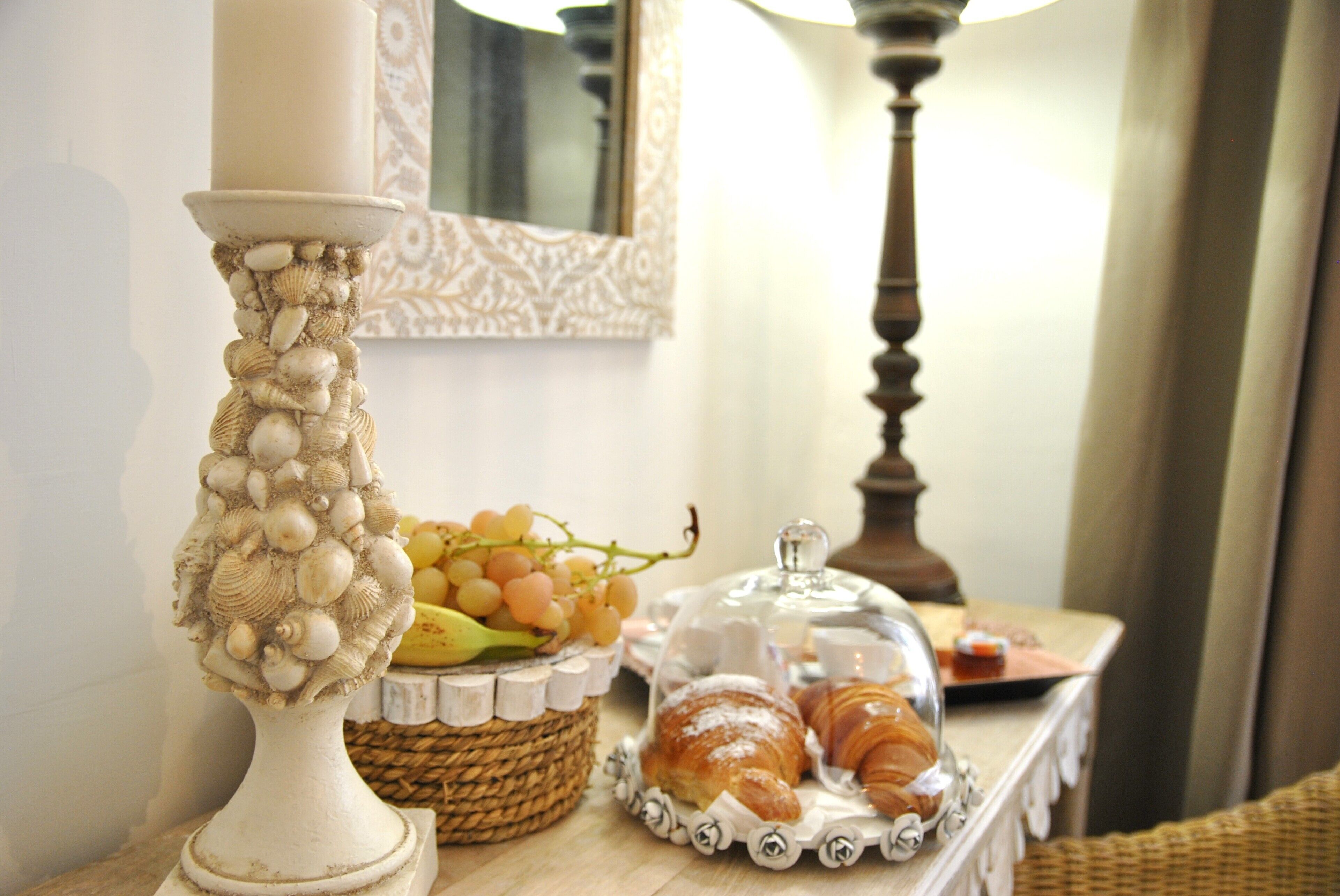 A table with a decorative lamp, a basket of grapes, and a tray of pastries.