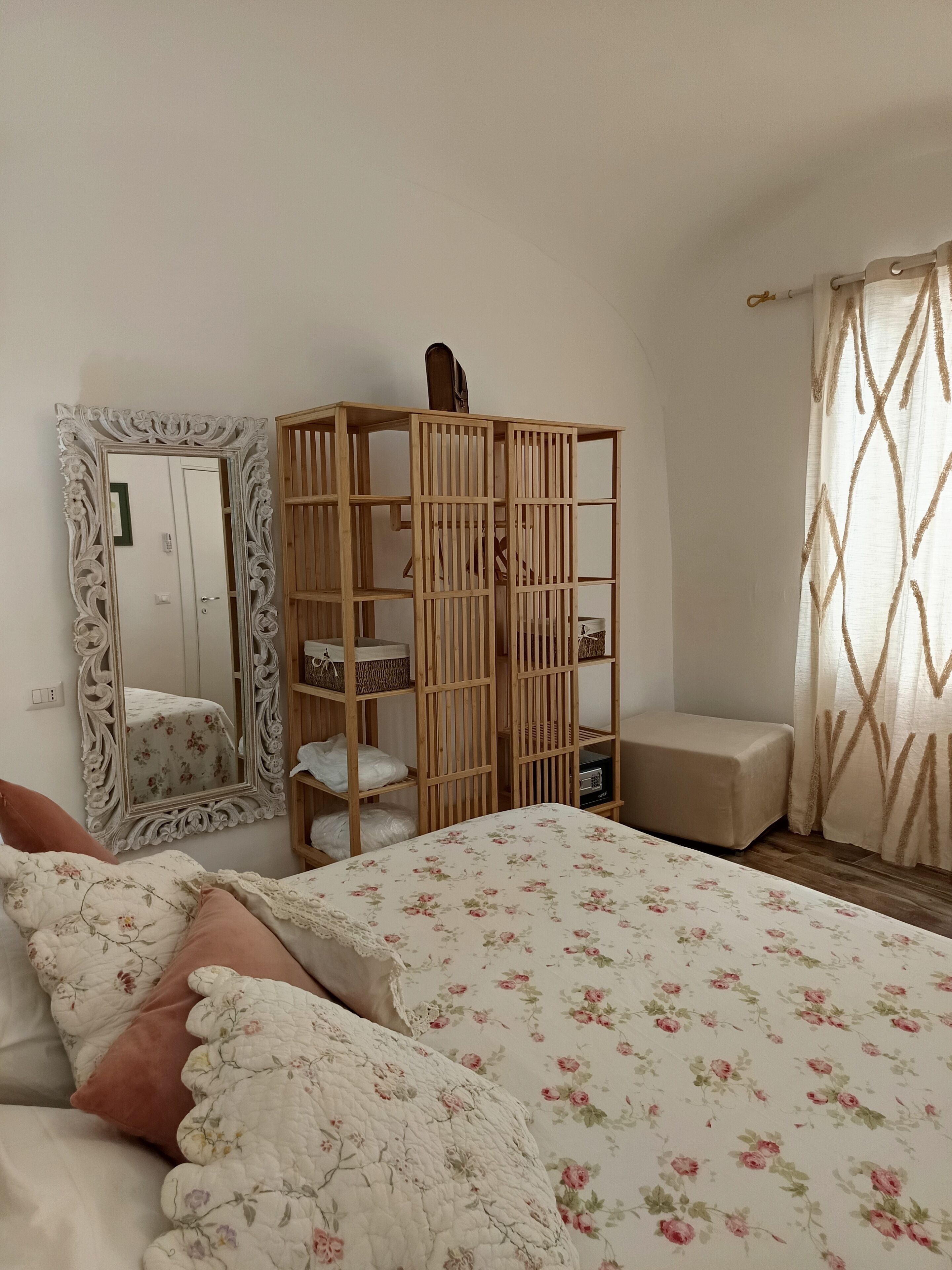 Ein Schlafzimmer mit Bett, Holzschrank, Spiegel und einem Fenster mit Vorhängen.