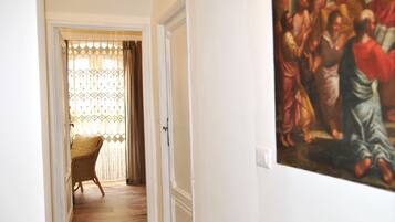 Un couloir avec un fauteuil en osier, une porte et un tableau accroché au mur.