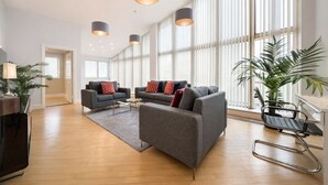 A spacious living area with grey sofas, a glass coffee table, and pendant lighting. - Roomspace -The Courtyard Penthouse (London)