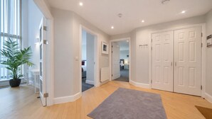 A modern hotel hallway with wooden floors, a grey rug, white doors, and a potted plant. - Roomspace -The Courtyard Penthouse (London)