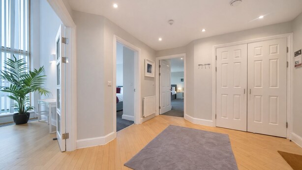 A modern hotel hallway with wooden floors, a grey rug, white doors, and a potted plant. - Roomspace -The Courtyard Penthouse (London)