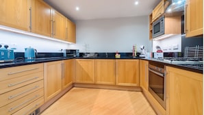 A modern kitchen with wooden cabinets, a black countertop, and stainless steel appliances. - Roomspace -The Courtyard Penthouse (London)