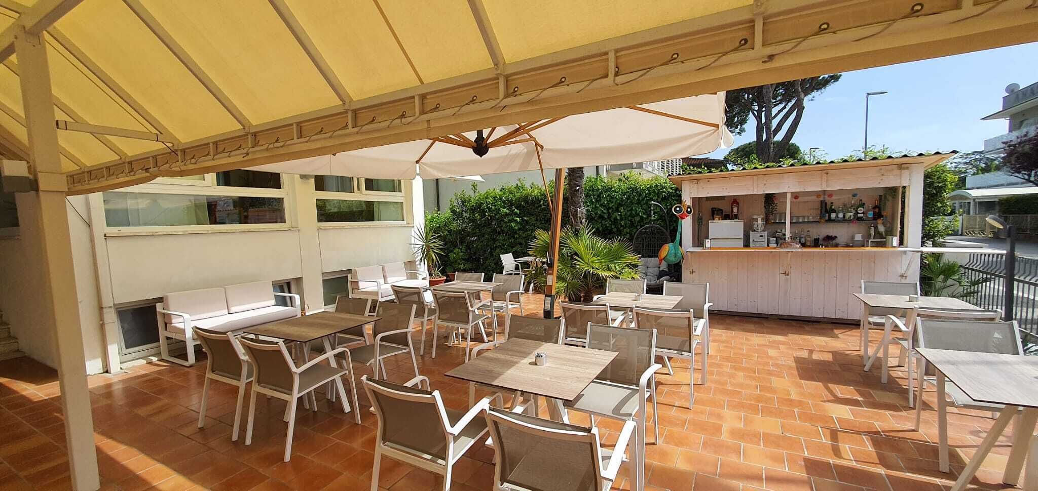 Una veranda esterna con diversi tavoli e sedie, un'area bar e una zona salotto coperta.