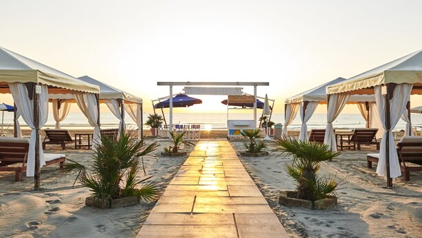 A beachside walkway leading to a canopy structure with beach chairs and umbrellas. - Hotel B&B Manuela (Cervia)