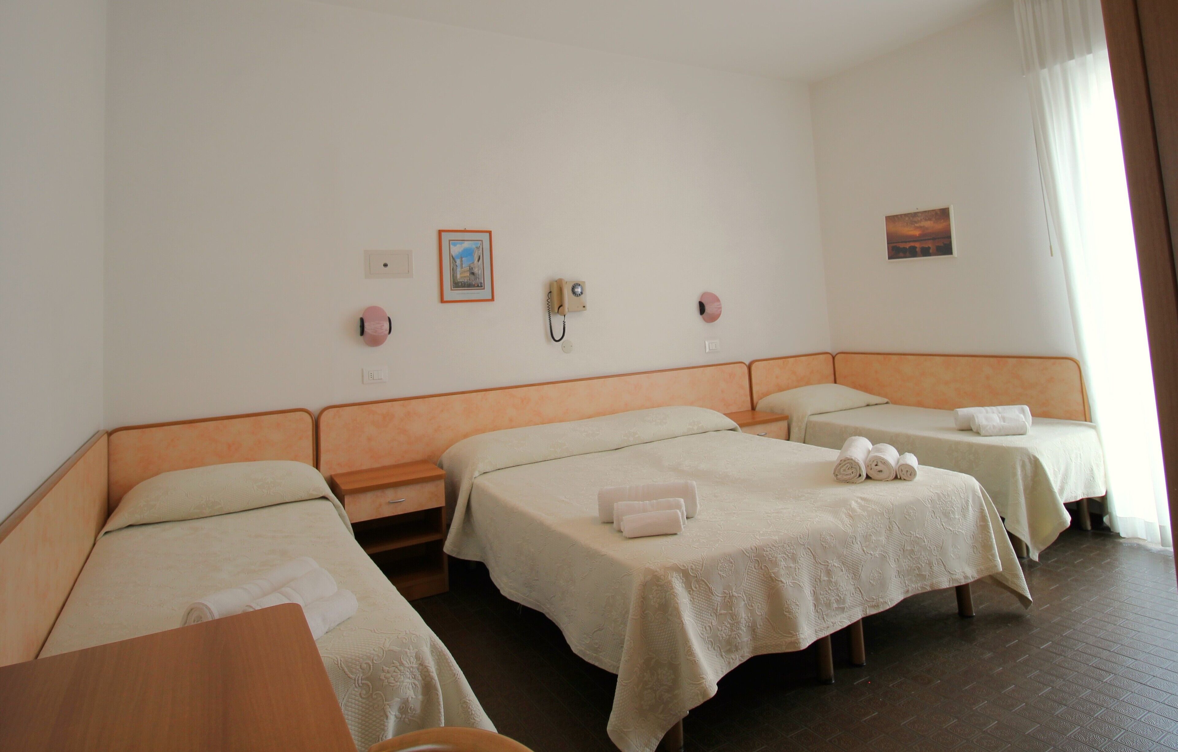 Habitación de hotel con tres camas individuales, una mesita de noche de madera, una pequeña mesa y un teléfono instalado en la pared.