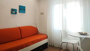 A room with a white sofa, a small white table with a bowl, and two blue wall art pieces. - Hotel B&B Manuela (Cervia)