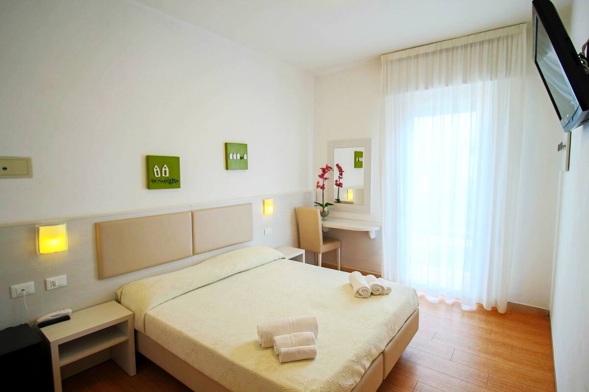 Hotellihuone, jossa on sänky, työpöytä, tuoli ja televisio.