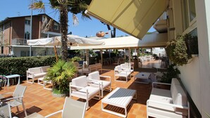 An outdoor patio area with white furniture, including sofas and chairs, and a tiled floor. - Hotel B&B Manuela (Cervia)
