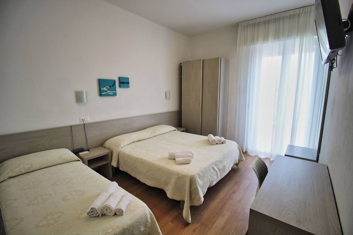 Hotellihuone, jossa on kaksi sänkyä, työpöytä ja vaatekaappi.