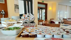 A buffet setup with various food items and beverages, including yogurt cups and packaged snacks, arranged on a table in a dining area. - Hotel B&B Manuela (Cervia)