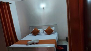 Un lit bien fait, avec du linge de lit blanc et des oreillers orange, une tête de lit blanche et une petite serviette blanche posée sur le lit.