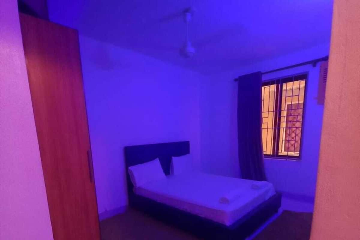 A room with a bed, a window with bars, and a door.