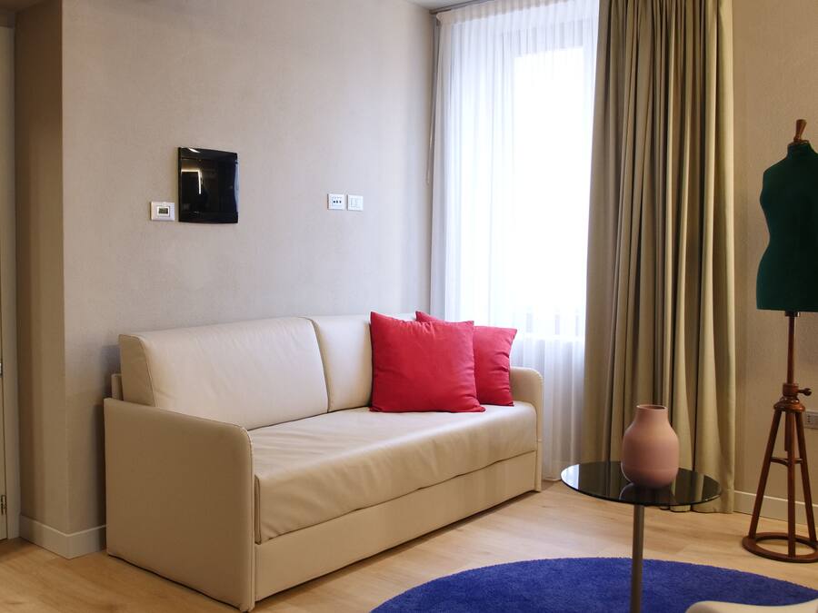 A room with a beige sofa, red pillows, a small round table, a vase, and two mannequins on stands.