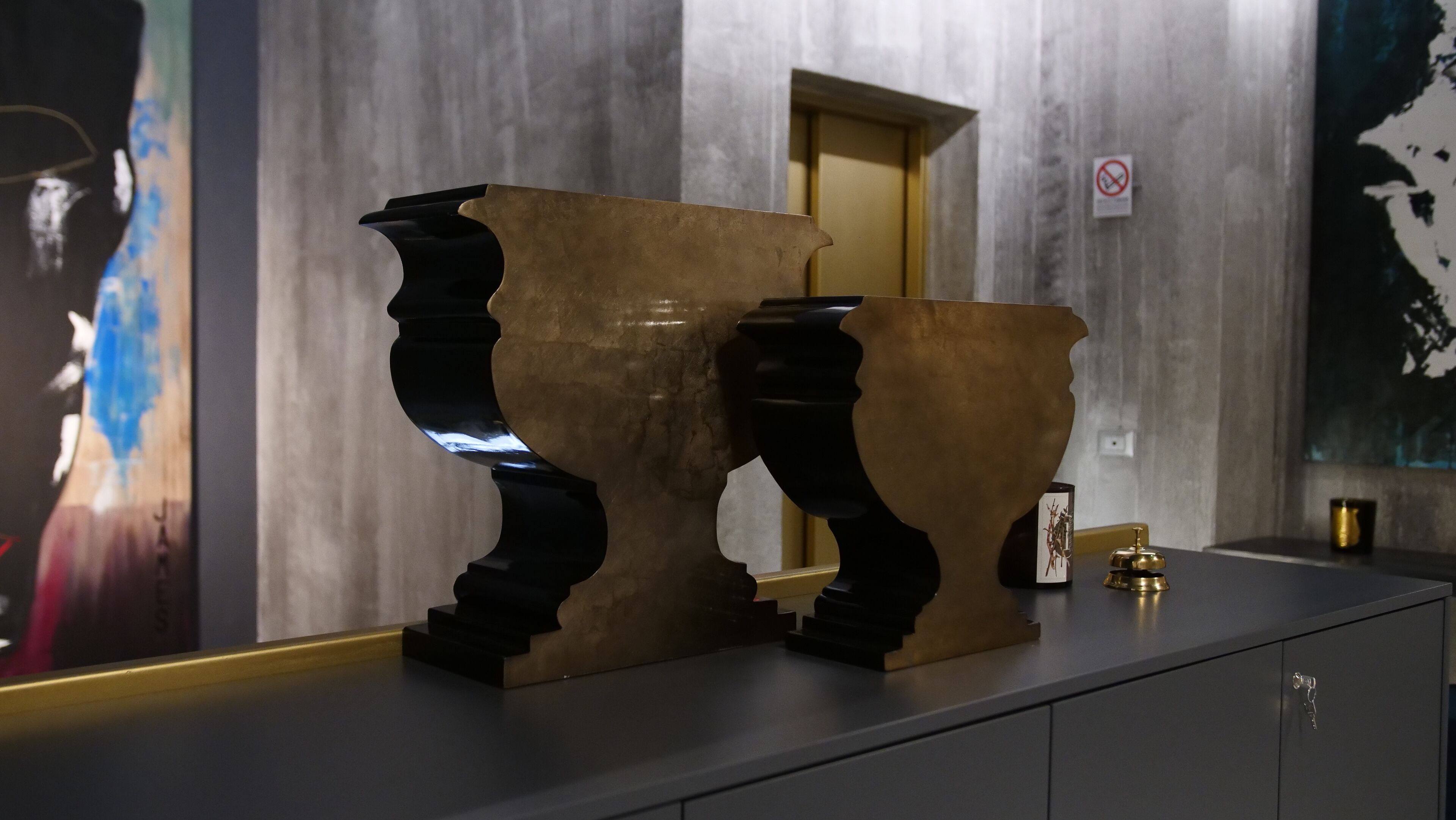 A modern interior with two abstract sculptures on a counter, a door in the background, and a no-smoking sign on the wall.