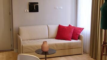 Ein modernes Wohnzimmer mit einem beigefarbenen Sofa, roten Kissen, einem weißen Sessel, einem kleinen Tisch mit einer Vase und einem blauen Teppich.