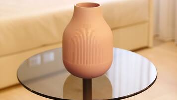 Um sofá bege com almofadas vermelhas, uma mesa de vidro com um vaso bege e um tapete azul.