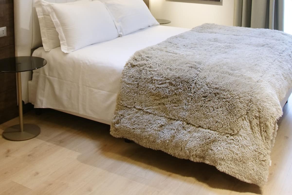 Une chambre moderne avec un grand lit, une tête de lit, une table de chevet, un tableau au mur et une fenêtre avec des rideaux.