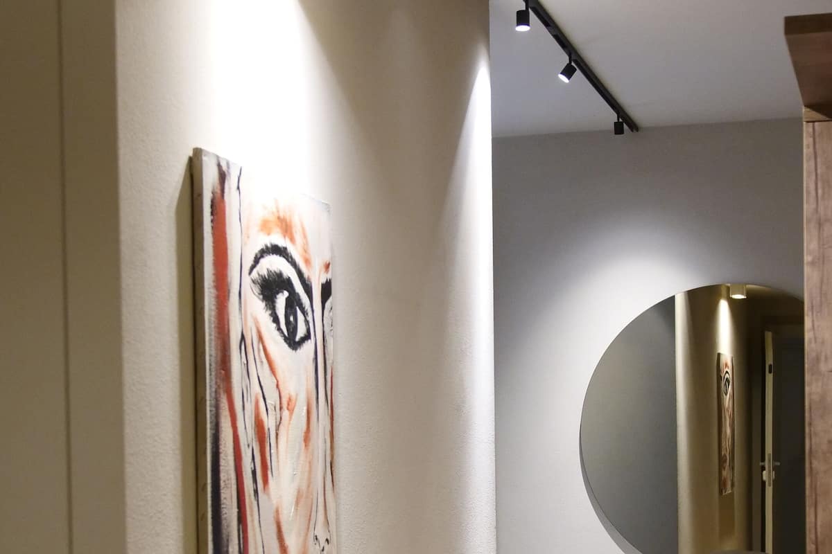Une chambre d’hôtel moderne au design minimaliste, avec un grand tableau abstrait au mur, un miroir rond et un lit doté d’une tête de lit en bois.