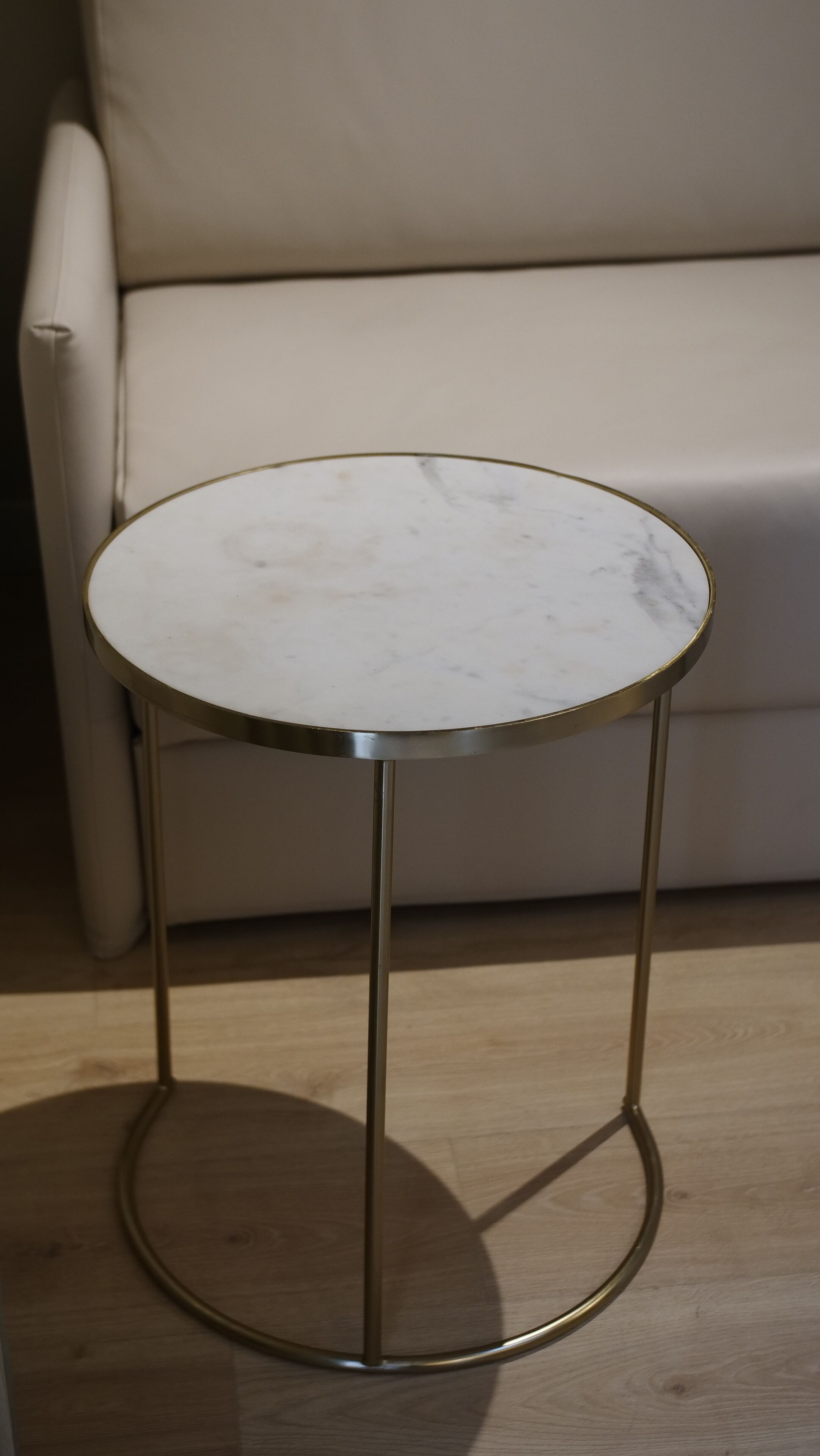 Een ronde tafel met een marmeren blad en gouden poten, staand op een houten vloer.