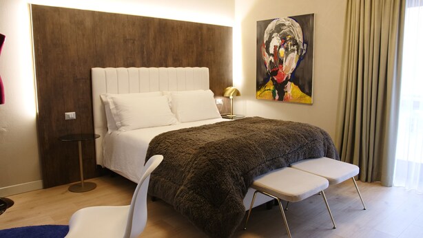 Een moderne slaapkamer met een groot bed, een nachtkastje met een lamp, een stoel en een schilderij aan de muur.