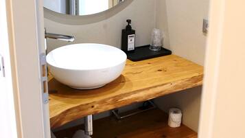 A bathroom with a white sink, wooden vanity, a round mirror, and a towel rack.