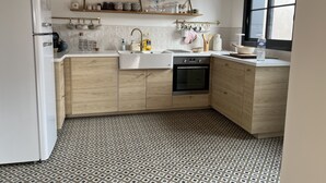 Een moderne keuken met een witte koelkast, houten kastjes, een inbouwoven en een groot raam.
