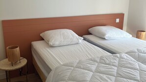 Een hotelkamer met twee bedden, een kleine ronde tafel met een lamp en een effen muur.