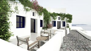 A white building with blue shutters, a stone-paved patio, and a view of the sea. - Superior Suite with Caldera View (Thira - Santorini)