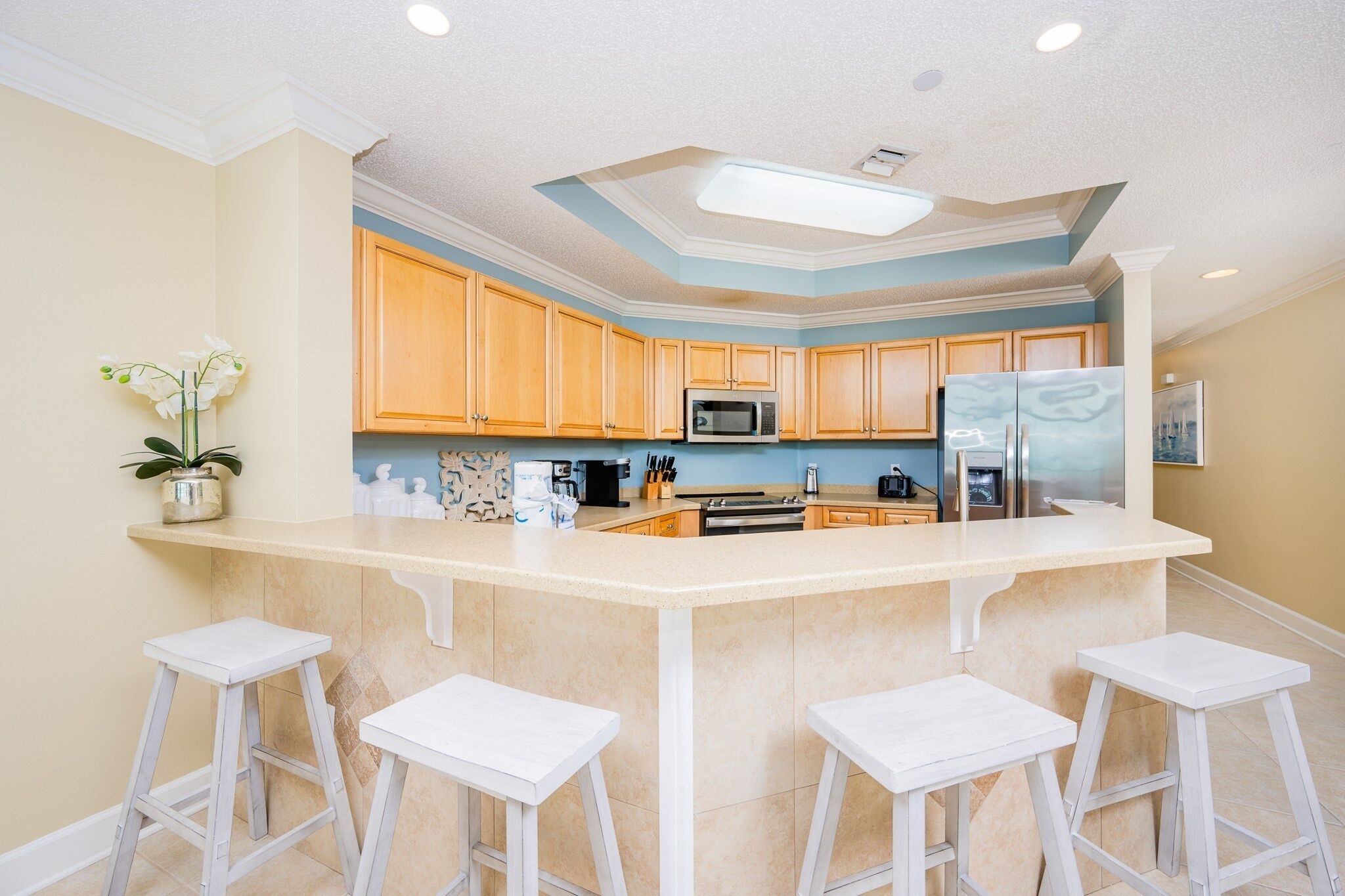 A kitchen with a central island, wooden cabinets, a microwave, a refrigerator, and bar stools.