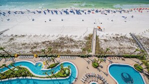 An aerial view of a beach resort with a large swimming pool, beach umbrellas, and lounge chairs.