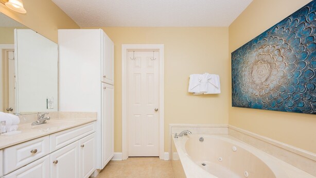 A bathroom with a white vanity, a bathtub, and a door with a towel hanging on it. - Phoenix West 1003 3 Bedroom Condo (Orange Beach)