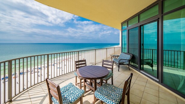 A balcony with a view of the beach, a table with chairs, and a yellow awning.