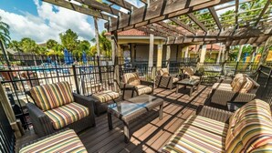 An outdoor patio area with wicker furniture and striped cushions, a glass-top table, and a view of a pool and palm trees. - Sunnyside Villa 6 Bedroom Home by RedAwning (Kissimmee)