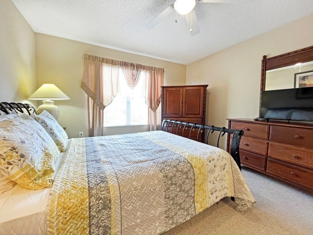 Une chambre à coucher comprenant un lit, une commode, une table de chevet, une lampe et un ventilateur de plafond.
