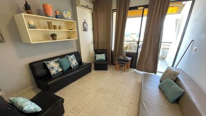 Un salon comprenant un canapé, un fauteuil, une petite table et une étagère ornée d’objets décoratifs.