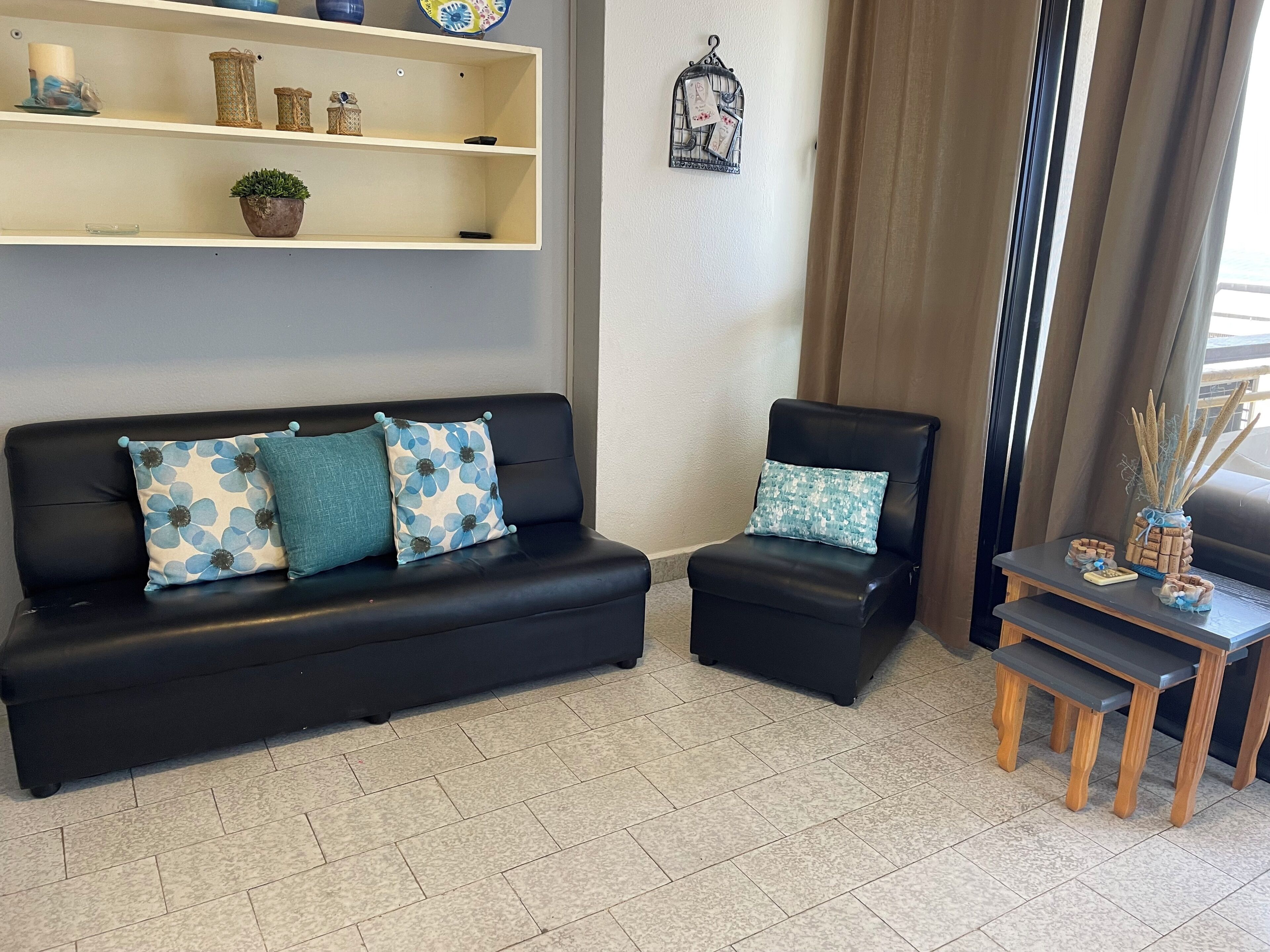 A living room with a black sofa, a matching armchair, a small wooden table, and a shelf with decorative items.