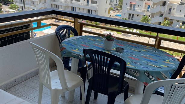 Un balcon avec une table et des chaises, un canapé blanc et une vue sur la mer et les bâtiments.