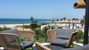 A balcony with wicker furniture, a small potted plant, and a view of the beach and ocean. - Hotel Boutique Aroma de Mar (Chiclana de la Frontera)