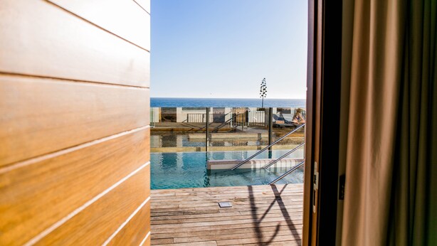 A wooden deck with a pool, a view of the sea, and a staircase leading to a lounge area. - Hotel Boutique Aroma de Mar (Chiclana de la Frontera)