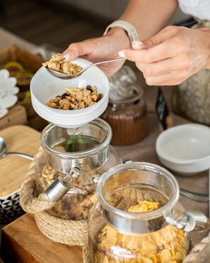 Una persona vertiendo granola desde un bol hacia un frasco de vidrio.