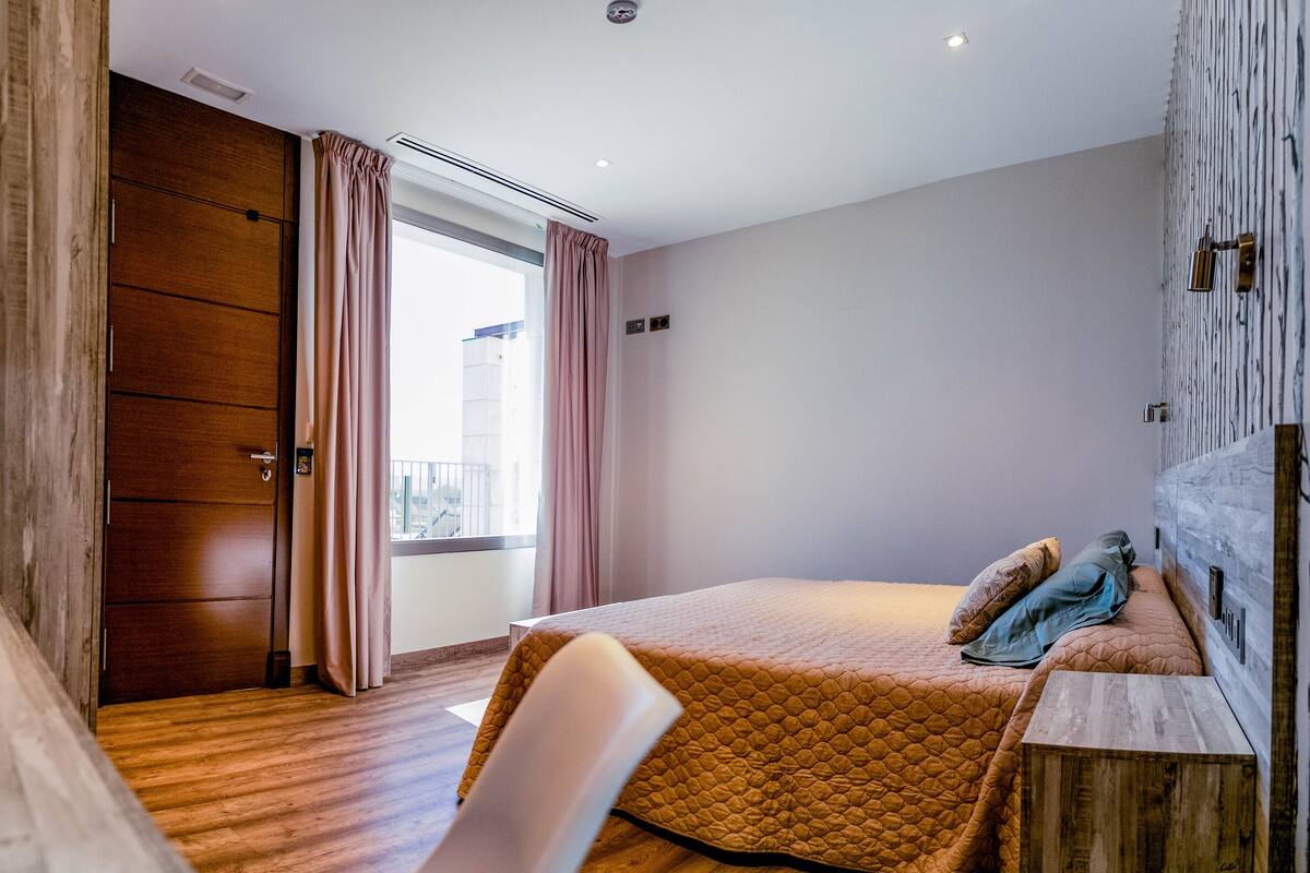 Une chambre d’hôtel avec un lit, un bureau en bois, une fenêtre avec des rideaux et une vue sur l’extérieur.