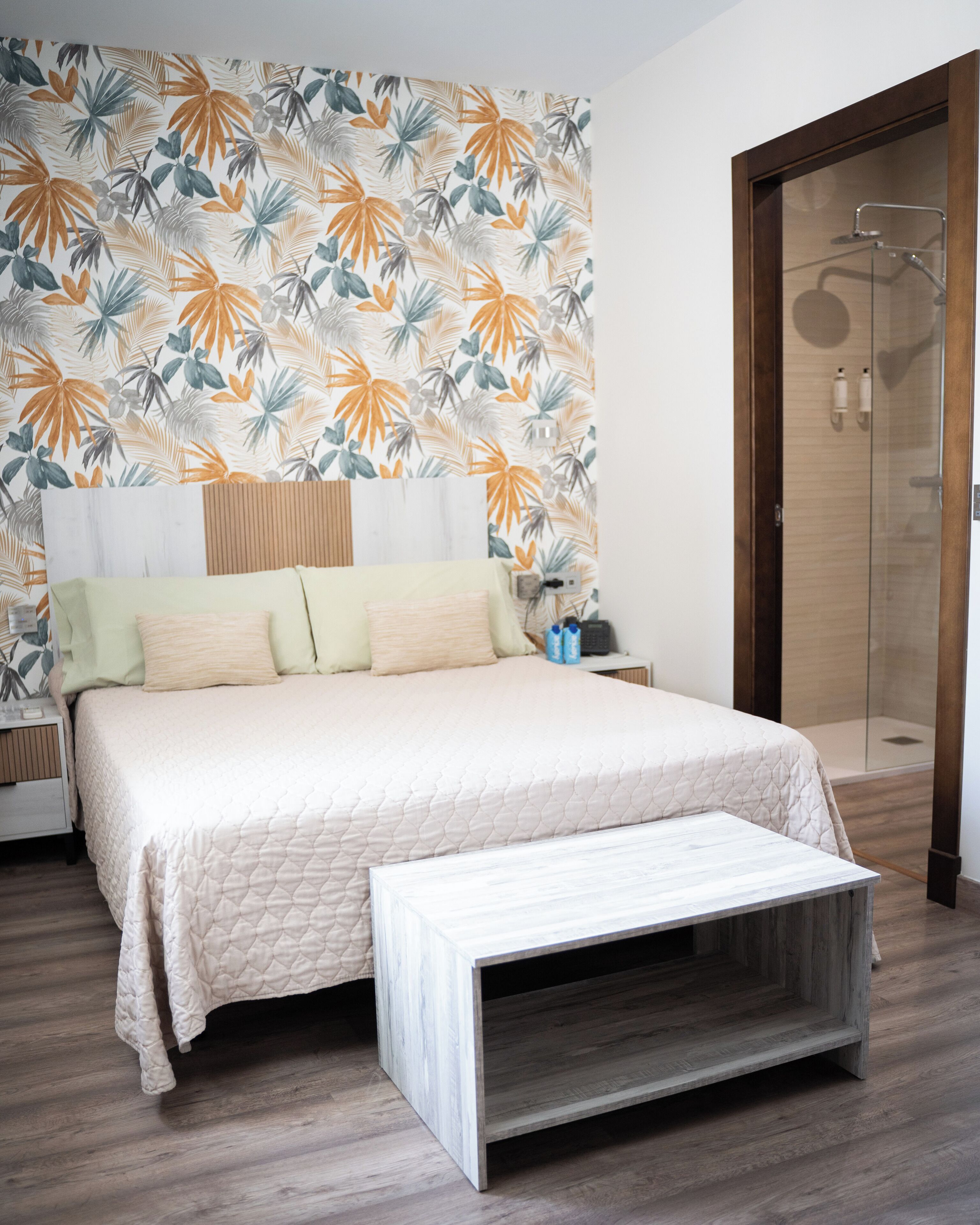 A bedroom with a bed, a nightstand, a bedside table, a wooden bench, and a shower area.