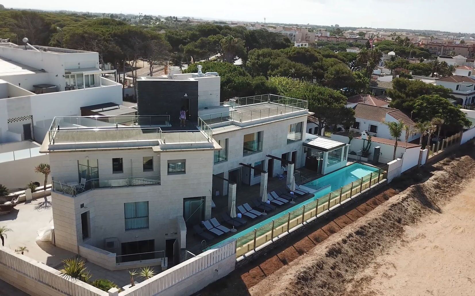 A modern two-story house with a rooftop terrace, a swimming pool, and a view of the surrounding neighborhood.